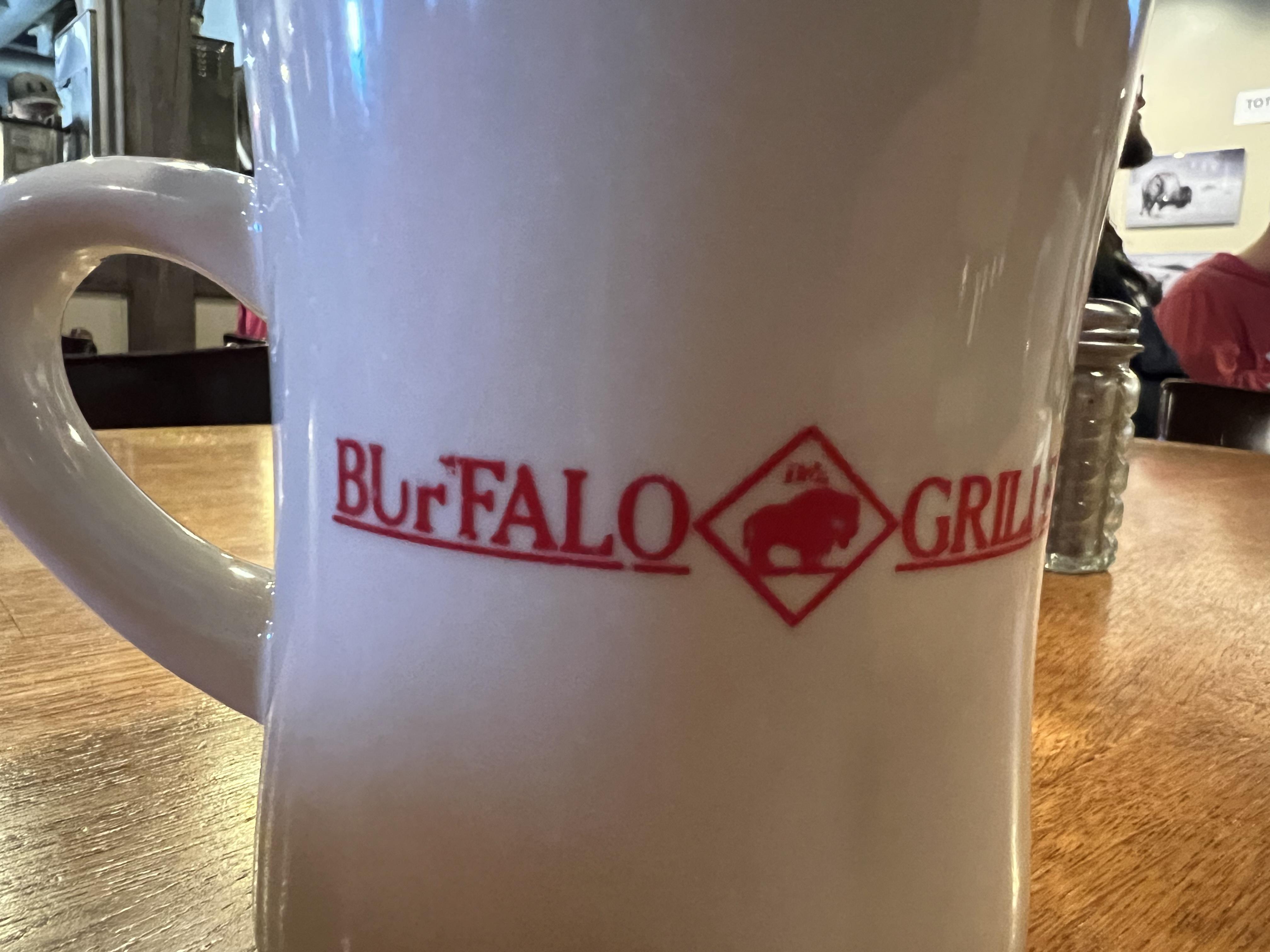 A coffee mug that says “Blurfalo Grille” and has a logo of the mighty blurfalo