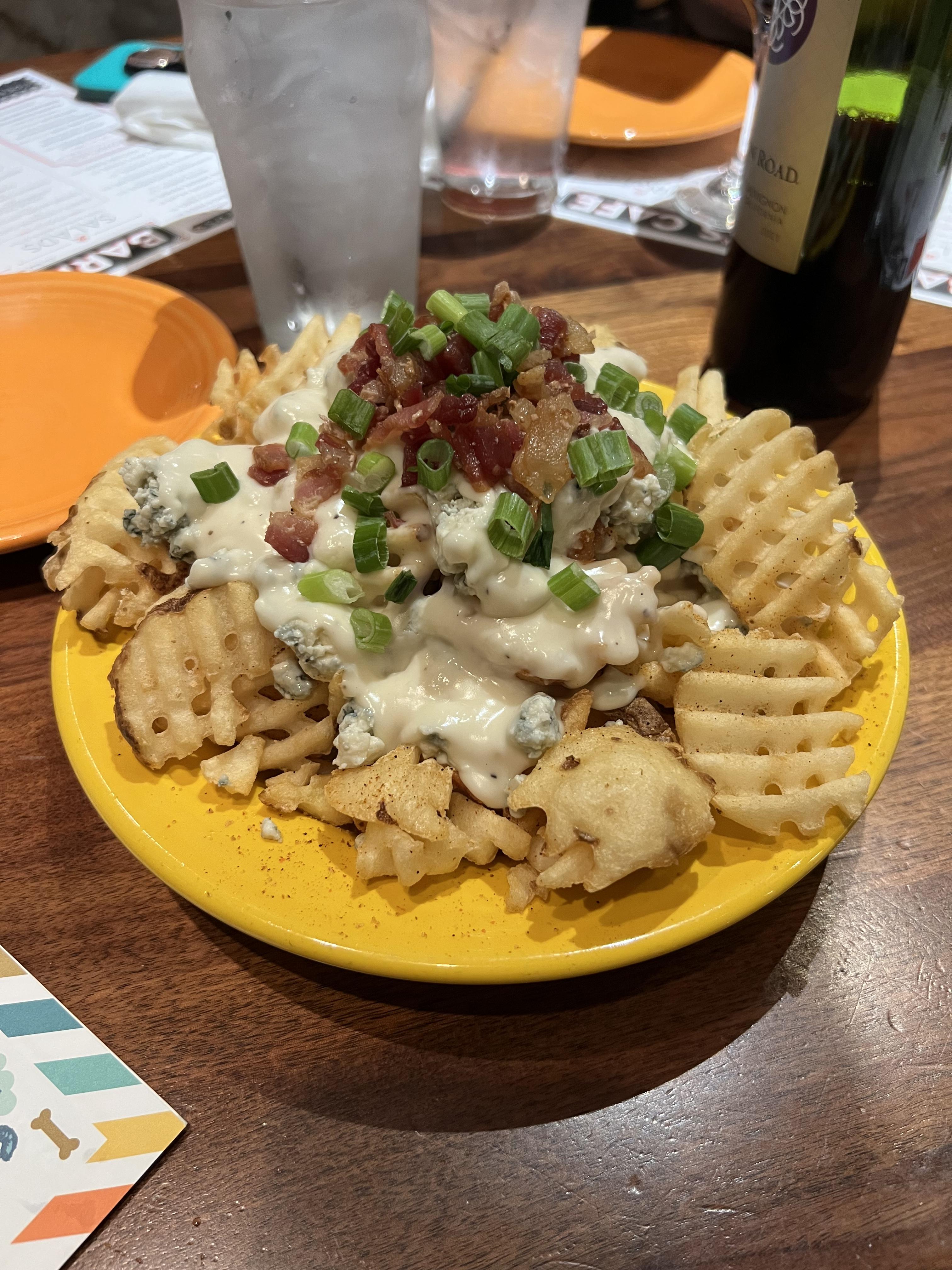 A bowl of waffle fries covered in delicious cheesy gravy, bacon, green onions, and bleu cheese crumbles